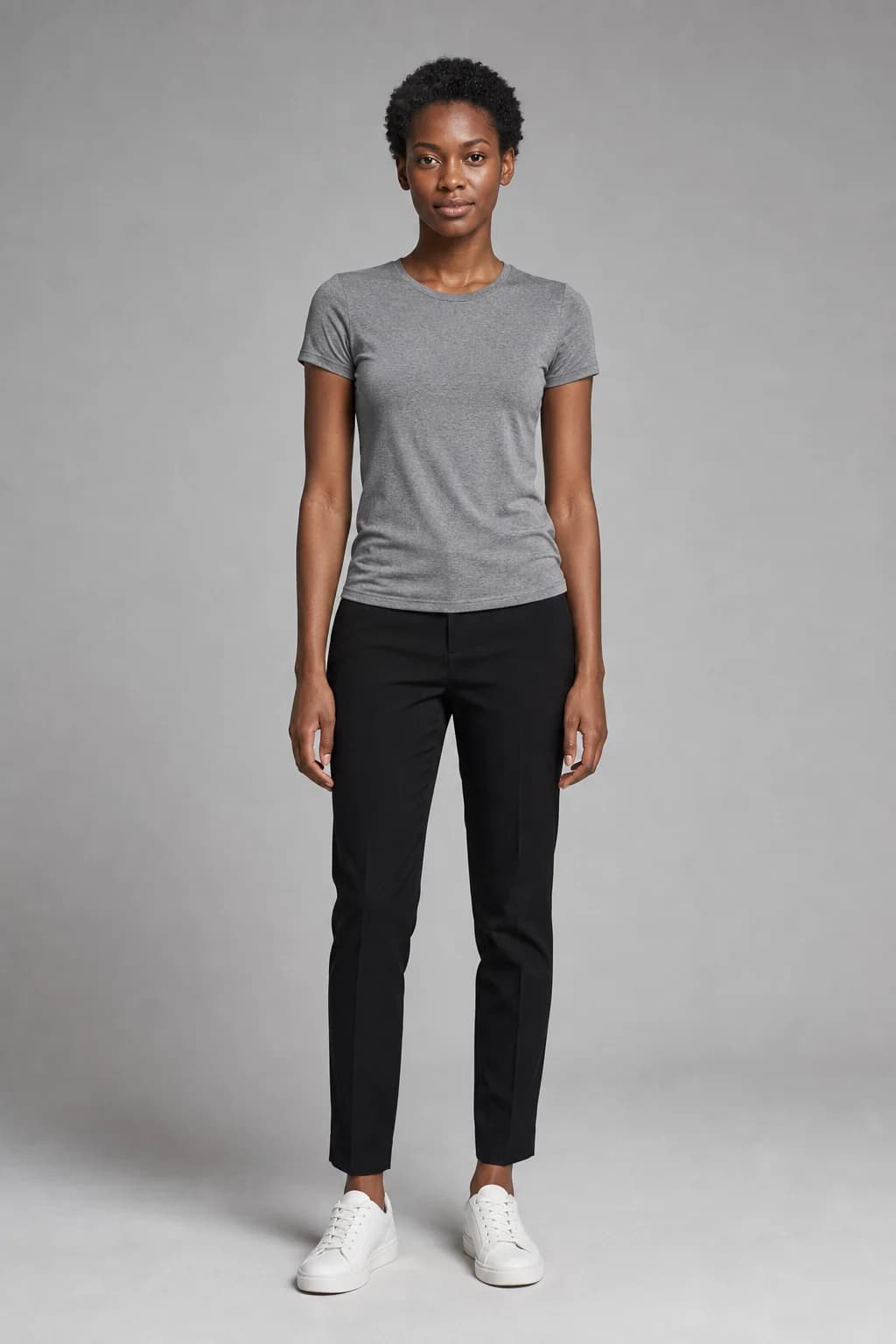 AI-generated house model reference: a woman with short natural hair in a grey T-shirt, black trousers and white trainers against a grey wall